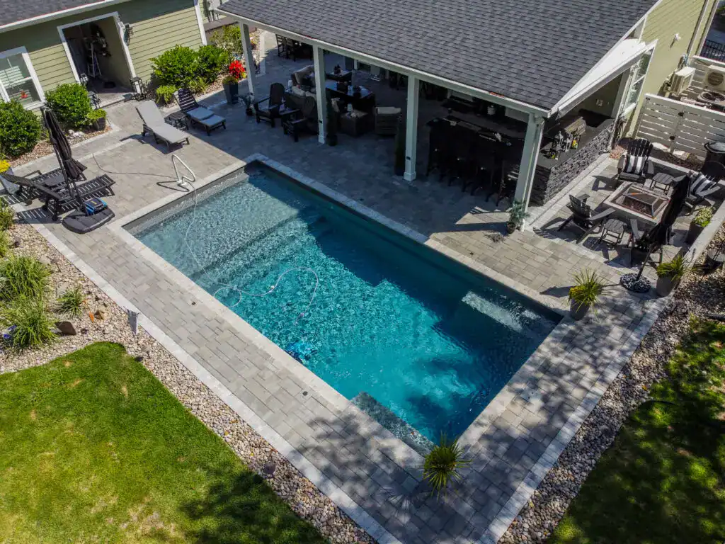 Elegant outdoor patio with a custom paver pool deck, seamless integration of swimming pool and entertainment area, surrounded by lush landscaping, perfect for backyard relaxation and outdoor gatherings.
