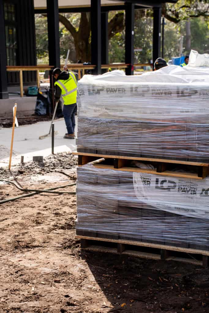 Instalación de adoquines para patio exterior utilizando materiales de alta calidad de Lowcountry Paver en una obra residencial. Los trabajadores colocan los cimientos con herramientas profesionales.