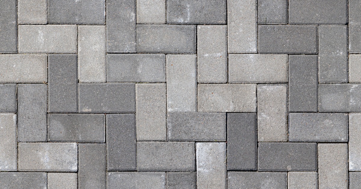 Gray pavers installed in the ground in a basket weave pattern. White smudges are scattered across the pavers.