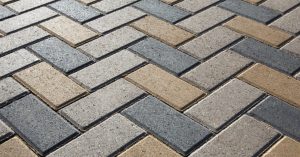 Driveway pavers installed in a herringbone pattern. The pavers are different shades of beige and charcoal.
