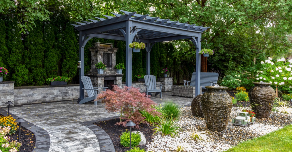 A large gray pergola installed on top of colorful patio pavers arranged in a mix of white and gray tiles.