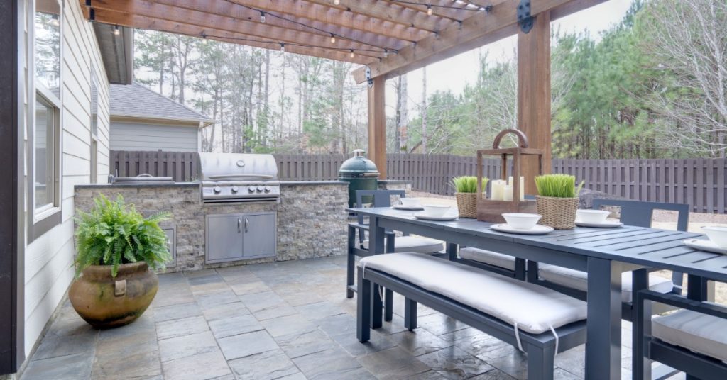 An arbor extending over a residential kitchen outside in a home’s backyard. The floor is made of square patio pavers.