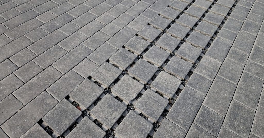 A strip of square permeable pavers installed in the center of a concrete paver floor during the daytime.