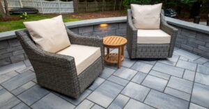 Two large chairs with cushions on a luxurious backyard patio made of concrete pavers behind a house.