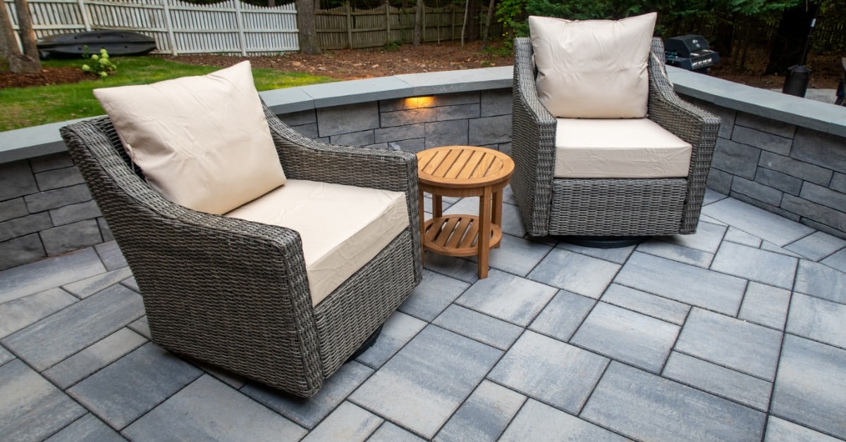 Two large chairs with cushions on a luxurious backyard patio made of concrete pavers behind a house.